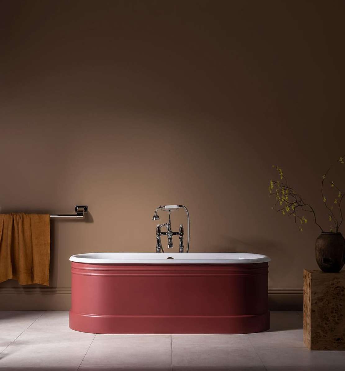 Red bathtub with white trim in a bathroom with brown walls and light tile flooring, complemented by a silver towel rack and wooden side table.