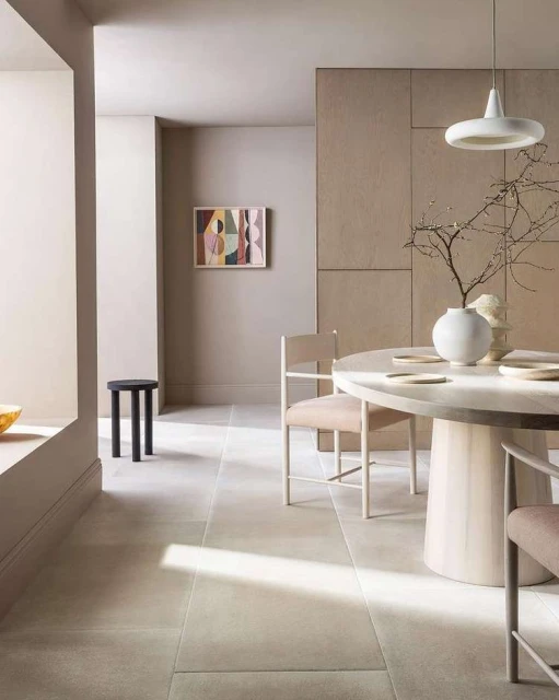 Beige dining room interior featuring a round table with chairs, pendant light, and minimalist decor with neutral tones and natural light.