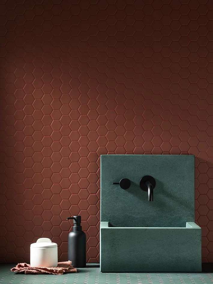 Minimalist bathroom design featuring a green concrete sink with black fixtures, complemented by a brown geometric tile wall and accessories.