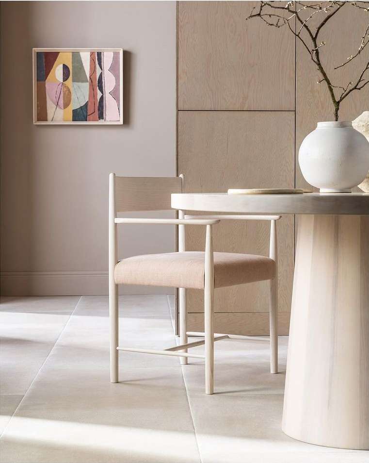Interior design featuring a round marble table, a minimalist chair, abstract wall art, a modern vase with twigs, and neutral color scheme.