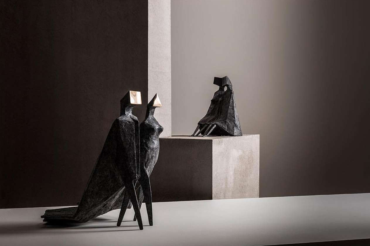 Three abstract figure sculptures of different heights and poses displayed on concrete blocks in a studio with neutral lighting.