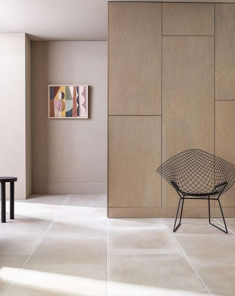 Interior view of an artful space with a wire chair, dark stool, light stone floor, and abstract painting.