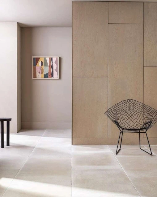 Interior view of an artful space with a wire chair, dark stool, light stone floor, and abstract painting.