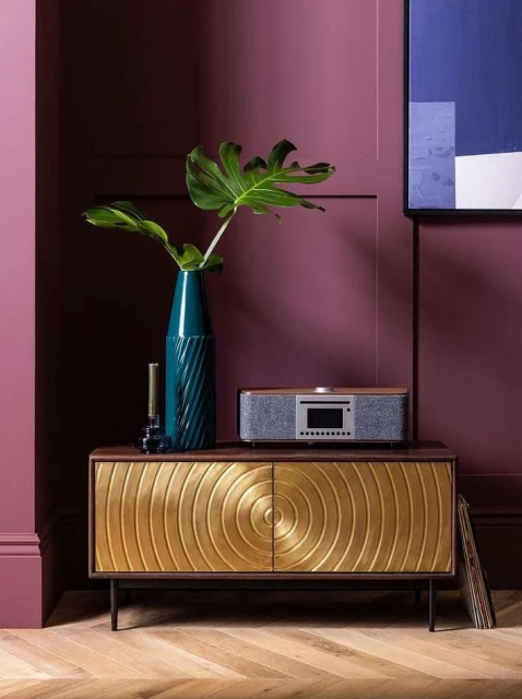 Stylish interior with a credenza featuring gold circular designs, a turquoise vase with Monstera leaves, and a modern audio system.