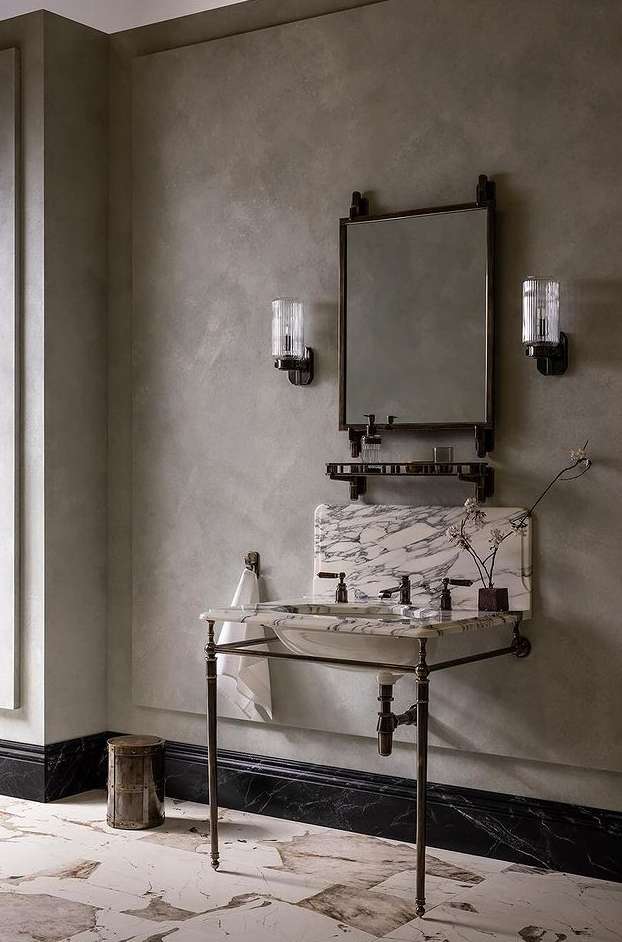 Bathroom interior featuring a marble vanity with a sink, a metal-framed mirror, and sconces, creating a refined and elegant space.