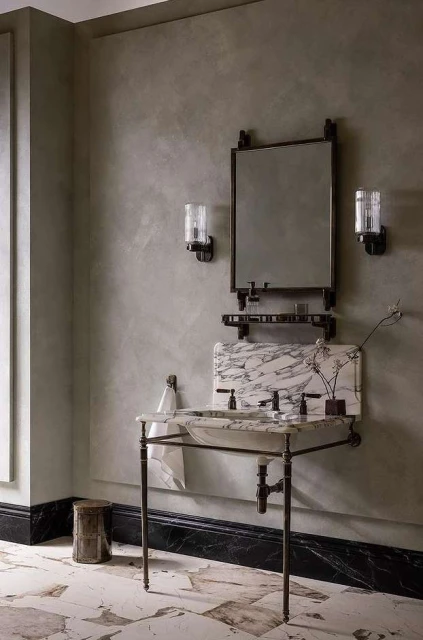 Bathroom interior featuring a marble vanity with a sink, a metal-framed mirror, and sconces, creating a refined and elegant space.