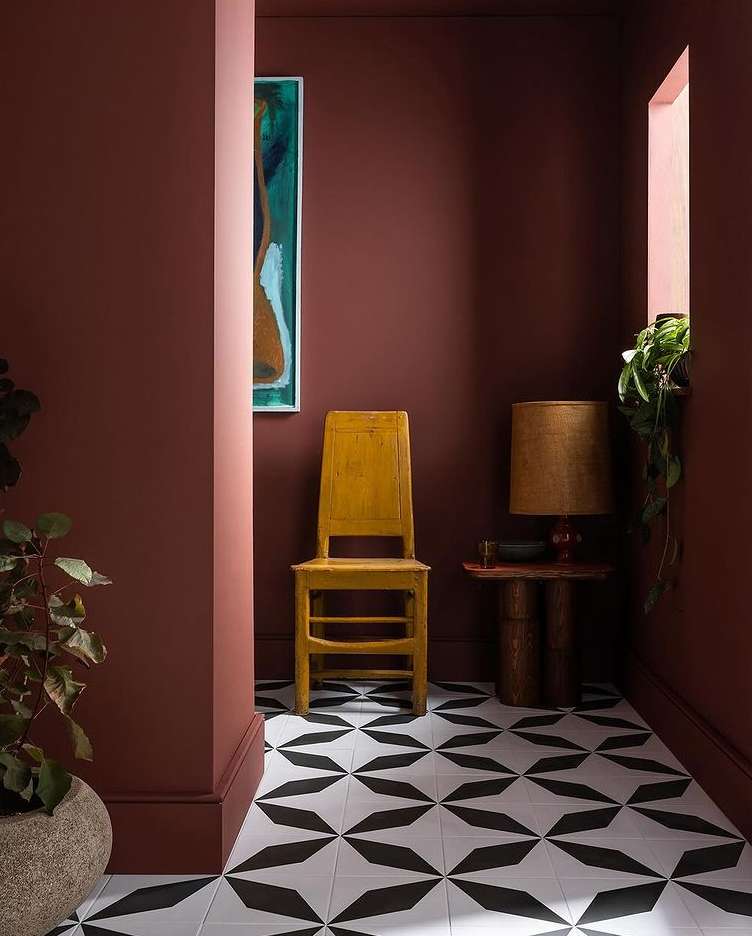 Yellow wooden chair against terracotta walls with geometric black and white tile flooring and a side table with lamp.