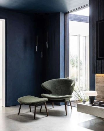 Modern living room interior featuring a green lounge chair with ottoman, dark blue walls, and natural light from a large window.
