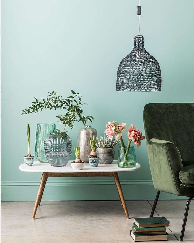 Interior decor featuring various plants in textured glass vases on a white table, set against a teal wall with a pendant lamp.
