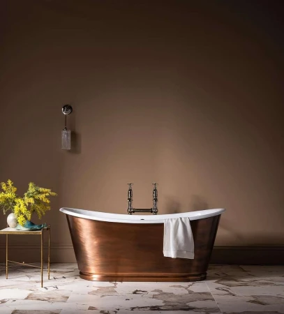Elegant bathroom interior featuring a copper bathtub with white towel, marble floor, and a vase of yellow flowers on a side table.