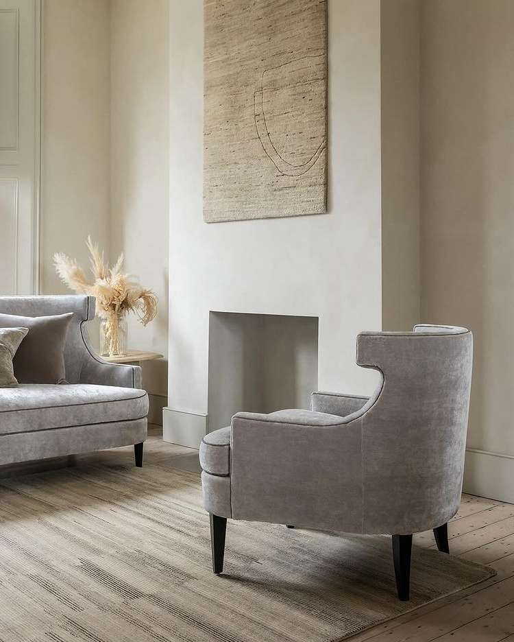 Living room interior featuring a gray upholstered armchair and loveseat, neutral walls, a textured area rug, and minimal decor.