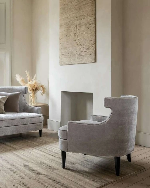 Living room interior featuring a gray upholstered armchair and loveseat, neutral walls, a textured area rug, and minimal decor.