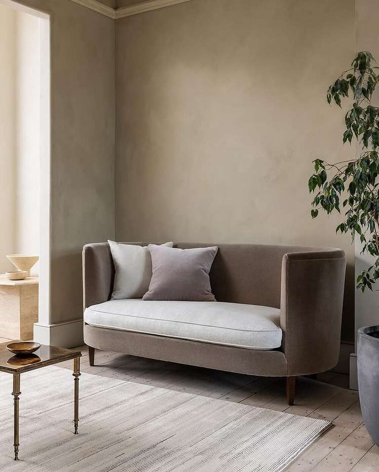 Indoor living room featuring a modern sofa with pillows, a glass-topped side table, neutral-toned walls, a light rug, and a potted plant.