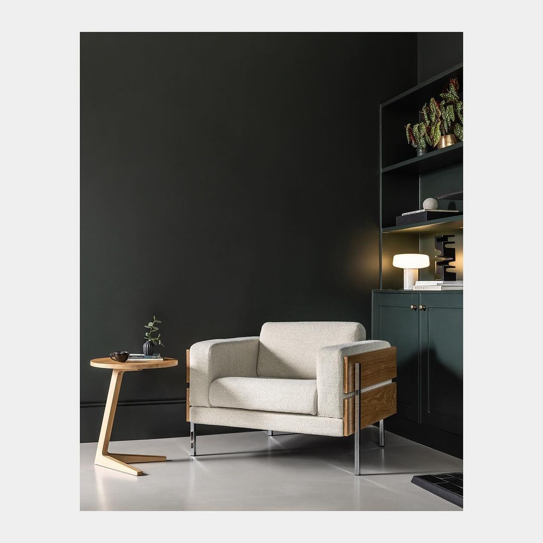 Beige armchair with wood accents and a wooden side table in a minimal, modern room with dark green walls and sleek, contemporary design.