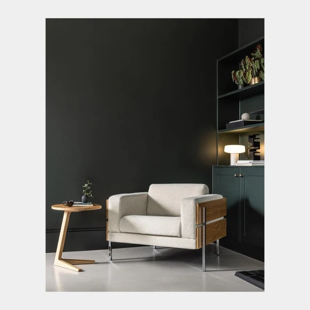 Beige armchair with wood accents and a wooden side table in a minimal, modern room with dark green walls and sleek, contemporary design.