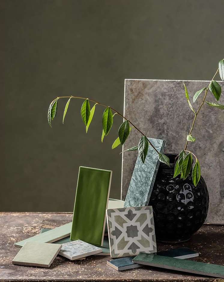 Still life composition featuring a collection of colorful tiles arranged with a plant stem and a dark vase on a textured surface.