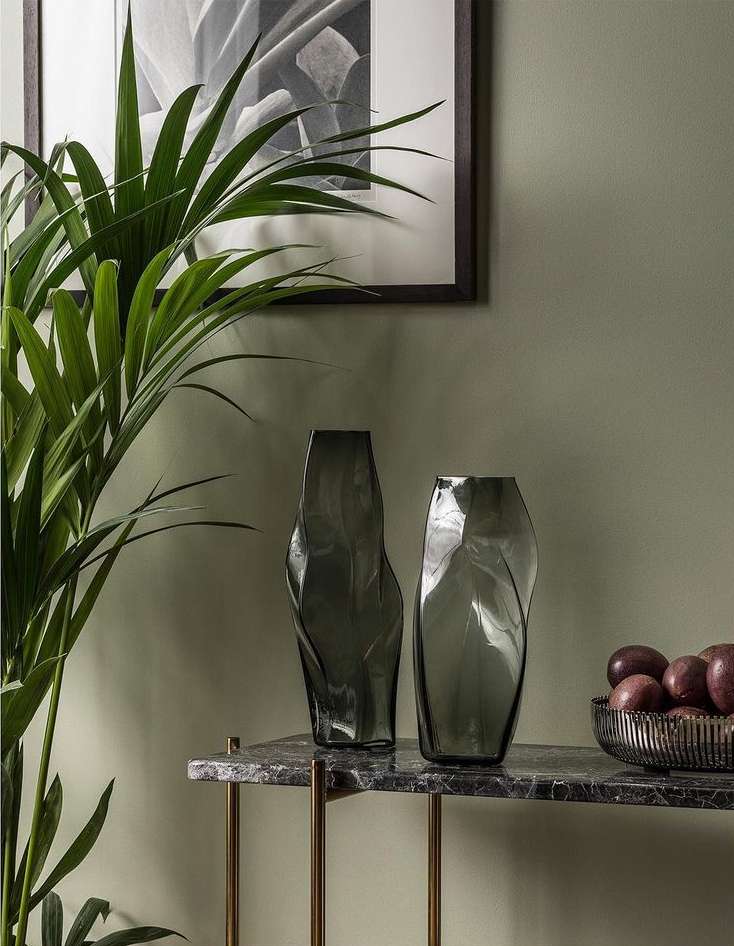 Two vases sit on a marble table with a plant and framed art in the background, creating an elegant interior design scene.