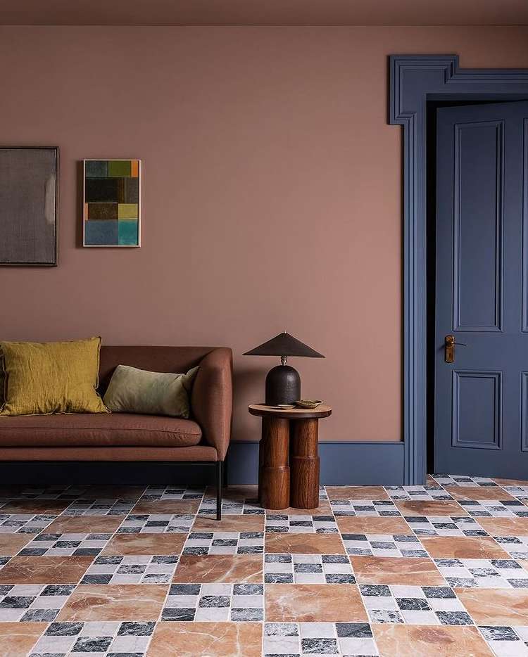 Living room interior featuring a brown sofa with yellow and green pillows, dark blue door, lamp on wooden table, and tiled floor.