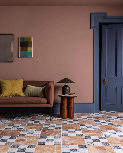 Living room interior featuring a brown sofa with yellow and green pillows, dark blue door, lamp on wooden table, and tiled floor.