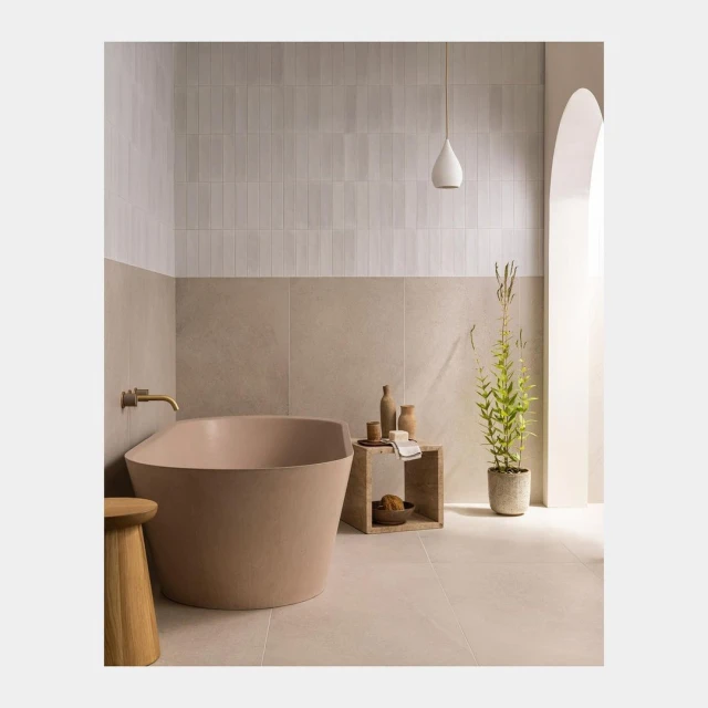 Bathroom interior featuring a standalone bathtub, stool, small side table with decorative items, and a potted plant in a neutral color scheme.