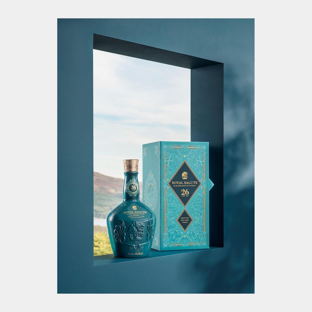 Royal Salute 26 Year Old Scotch Whisky bottle with packaging in a blue frame against a blurry landscape, promoting luxury spirits.