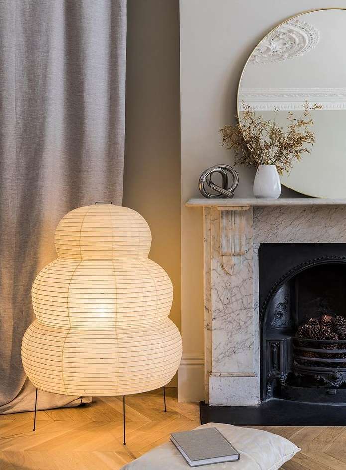 Interior view of a living room featuring a Japanese paper lantern floor lamp, fireplace, mirror, and neutral color palette creating a cozy ambiance.