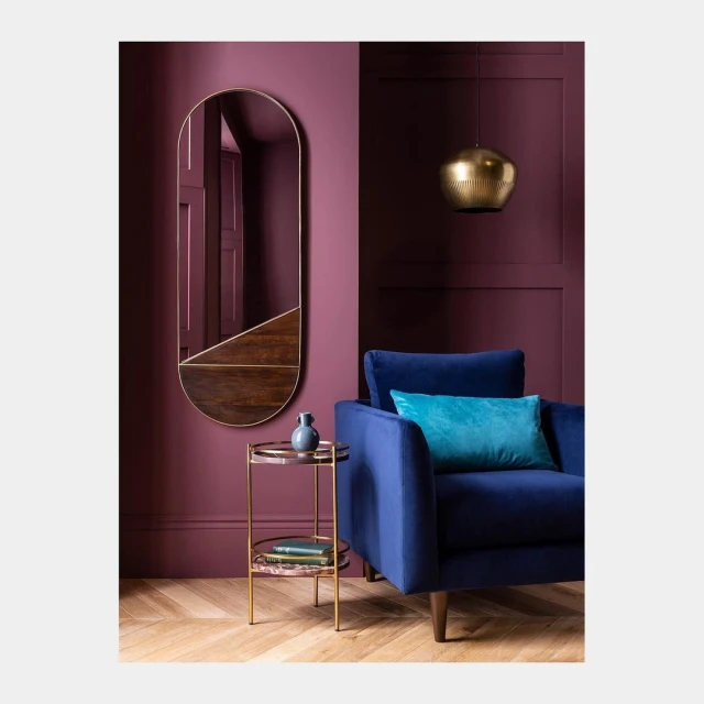 Interior design featuring a blue armchair, gold side table, hanging light fixture, and a stylish mirror against a plum-colored wall.