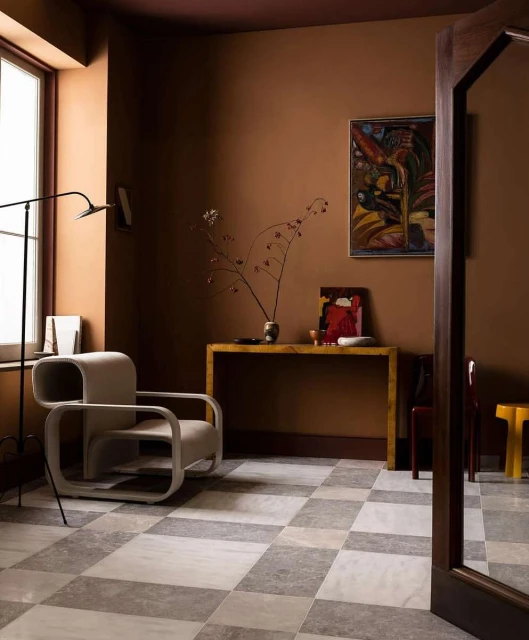 Interior view of a living space with a contemporary armchair, wooden console table, and checkered tile floor. Walls are painted in earth tones.