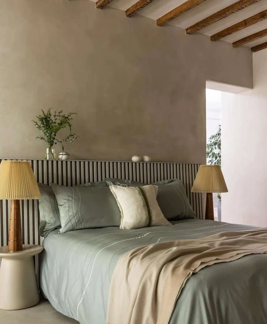 Bedroom interior featuring a bed with sage green bedding and wooden headboard, a side table with a lamp, and neutral-toned walls.