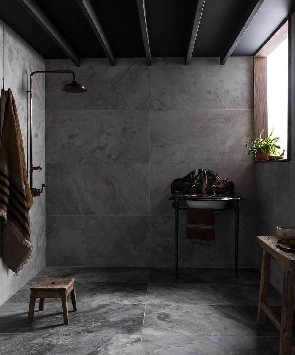 Rustic bathroom interior with stone walls, open shower, stool, antique sink, and wooden ceiling beams creates a minimalist aesthetic.
