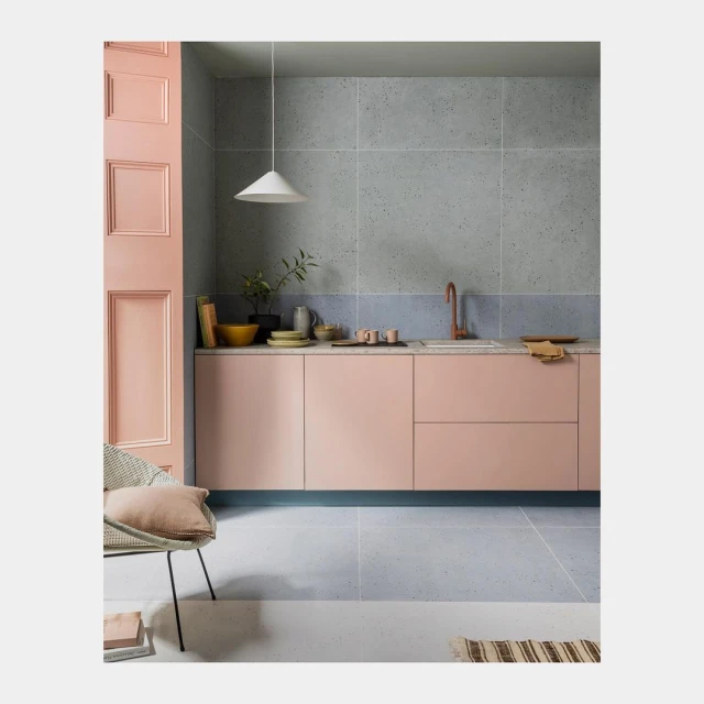 Modern kitchen interior featuring pink cabinets, concrete wall, and a white pendant light, showcasing a contemporary design aesthetic.
