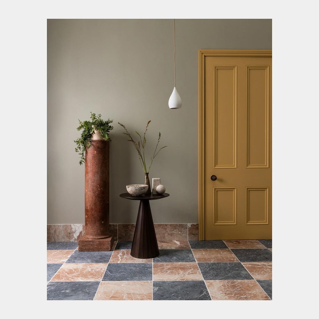 Interior design featuring a mustard-colored door, dark wood table, marble column with plant, and geometric-patterned marble tile floor.