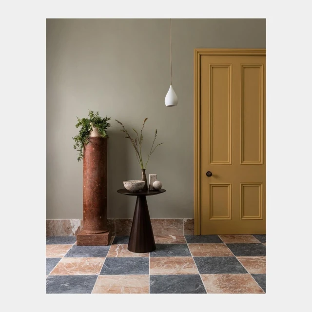 Interior design featuring a mustard-colored door, dark wood table, marble column with plant, and geometric-patterned marble tile floor.