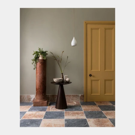 Interior design featuring a mustard-colored door, dark wood table, marble column with plant, and geometric-patterned marble tile floor.