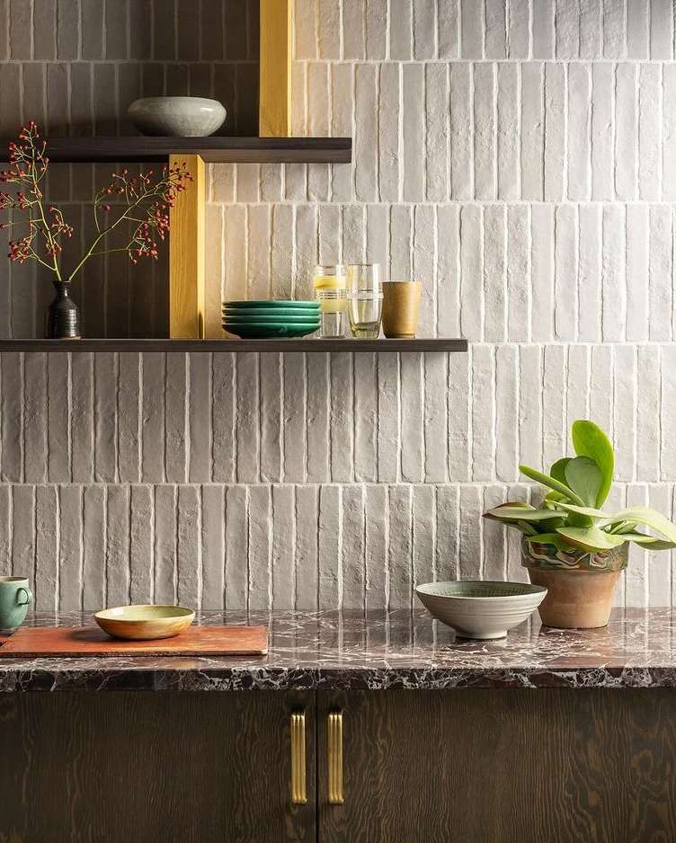 Interior design featuring a kitchen backsplash with vertical tiles, dark wood cabinetry, marble countertops, and decorative shelves.