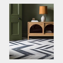 Interior shot featuring a wooden cabinet with arched glass doors, an orange lampshade, a green paneled door, and a chevron marble floor.