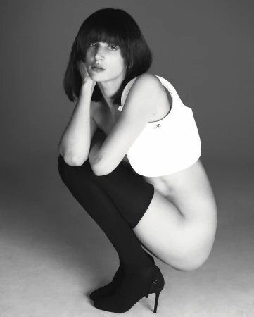 Black and white shot of a fair-skinned woman with black hair crouching, wearing thigh-high stockings, heels, and a small white bag.