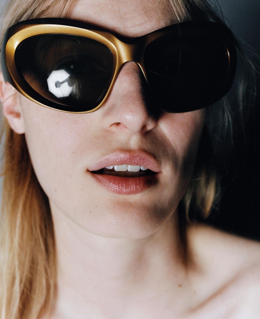 Close-up portrait of a blond woman wearing large gold sunglasses, emphasizing beauty, fashion, and portrait photography with studio lighting.
