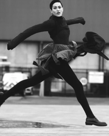 Black and white portrait of a woman captured mid-air jumping outdoors with dark clothing and a blurred background
