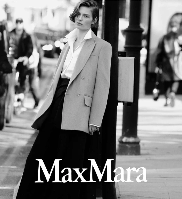Monochrome fashion shot: woman in blazer & wide-leg pants, city background. Max Mara logo visible at bottom. Editorial, sophisticated.