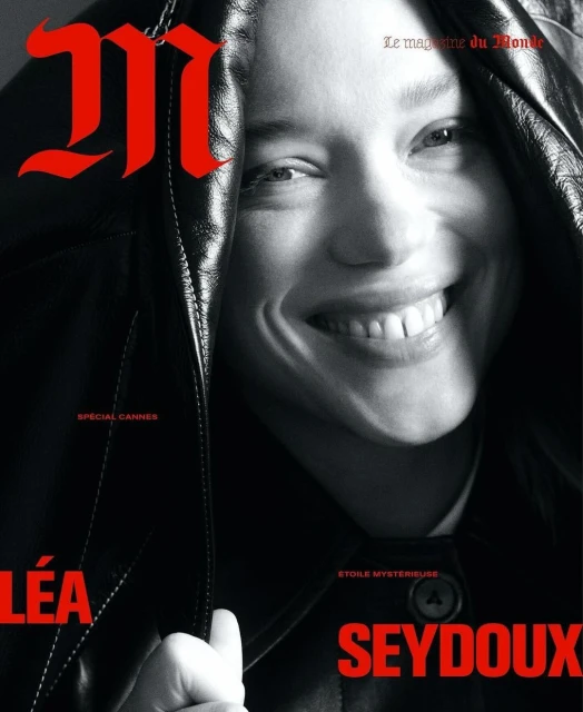 Black-and-white magazine cover featuring Léa Seydoux smiling, with red title text, a black leather jacket draped over her head and shoulders.