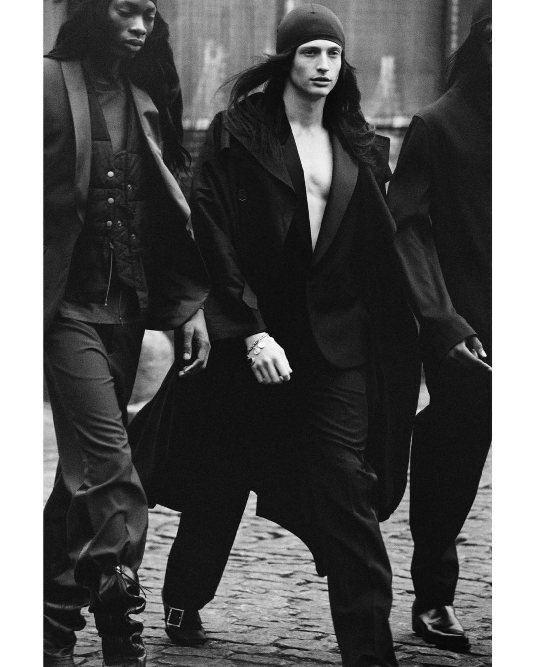 Black and white fashion shot of three young adult models walking on a city street wearing stylish formal wear and beanie cap.