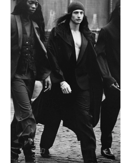 Black and white fashion shot of three young adult models walking on a city street wearing stylish formal wear and beanie cap.