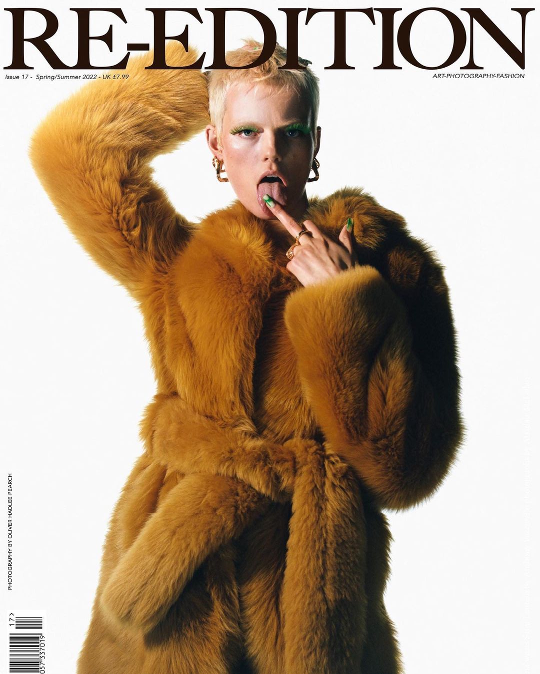 Magazine cover featuring a fair-skinned adult female with blonde hair wearing a fur coat and jewelry, sticking her tongue out.