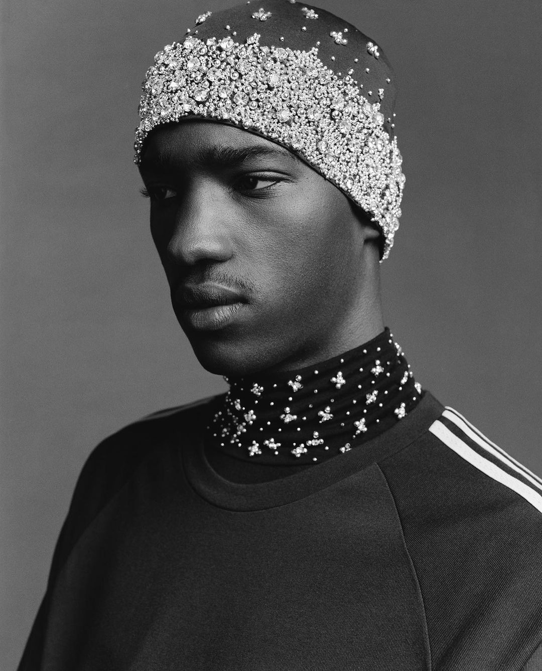 Close-up of Black male fashion model with beaded cap and neckpiece in a studio setting with even lighting on a neutral background.