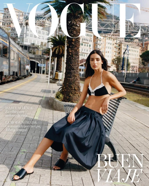 Vogue Espana cover featuring a woman in a black and white bikini top and navy skirt sitting on a bench at a train station.