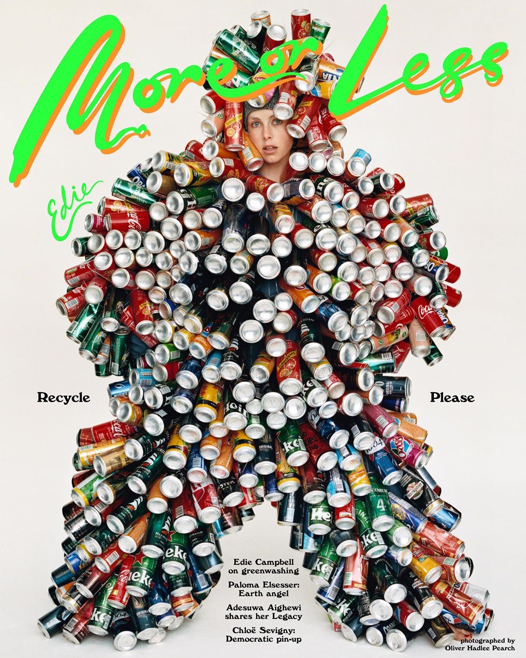 Adult female poses in a tan studio wearing a full body suit entirely made from crushed soda cans and with the text 'More or Less'.