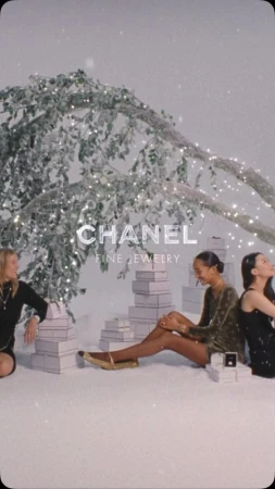 Three women sit among stacked gift boxes near a tree with fairy lights in a holiday-themed fashion and jewelry advertisement.
