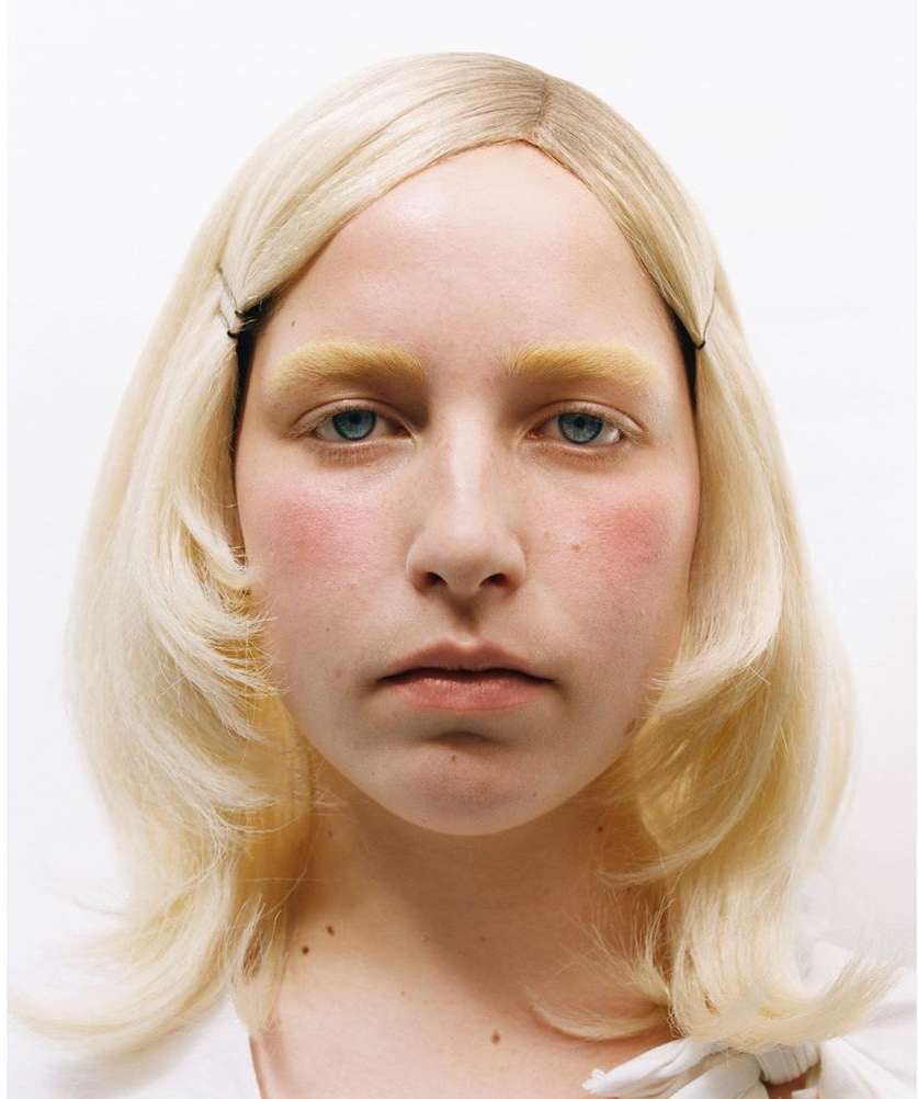 Headshot portrait of a woman with platinum blonde hair, blue eyes, and fair skin in front of a plain white background. Hair clips visible.