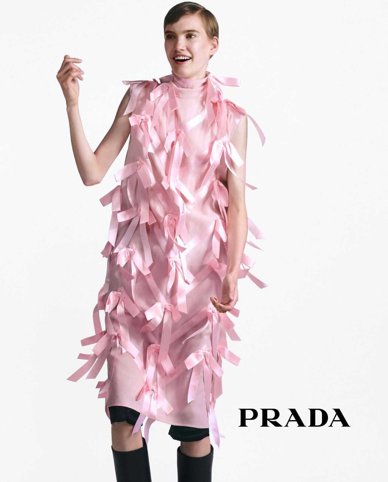 Model in pink ribbon dress wearing black boots standing against a white backdrop